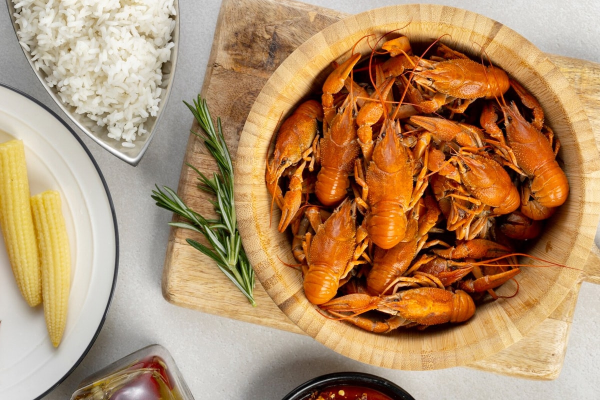 Top look of a wooden bowl with boiled crawfish sitting on a wooden cutting board.