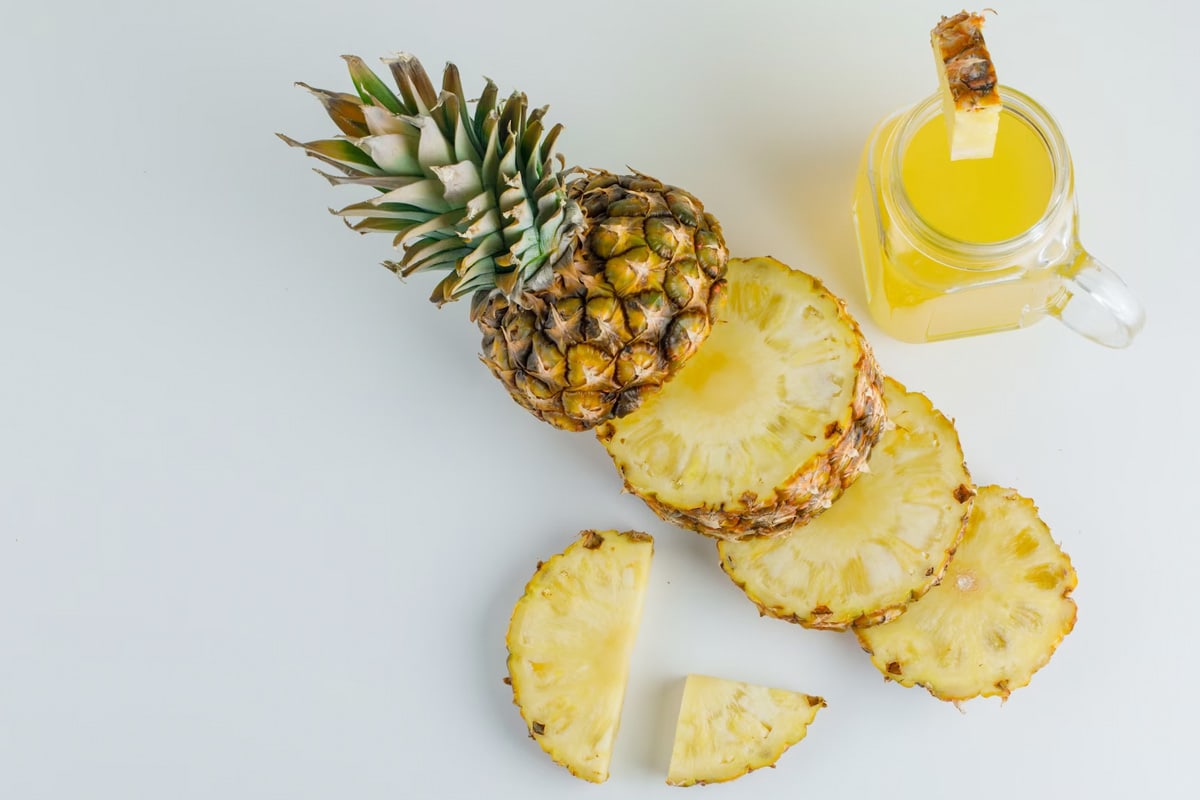 Top view of a few fresh pineapple slices near a transparent jar with pineapple juice.