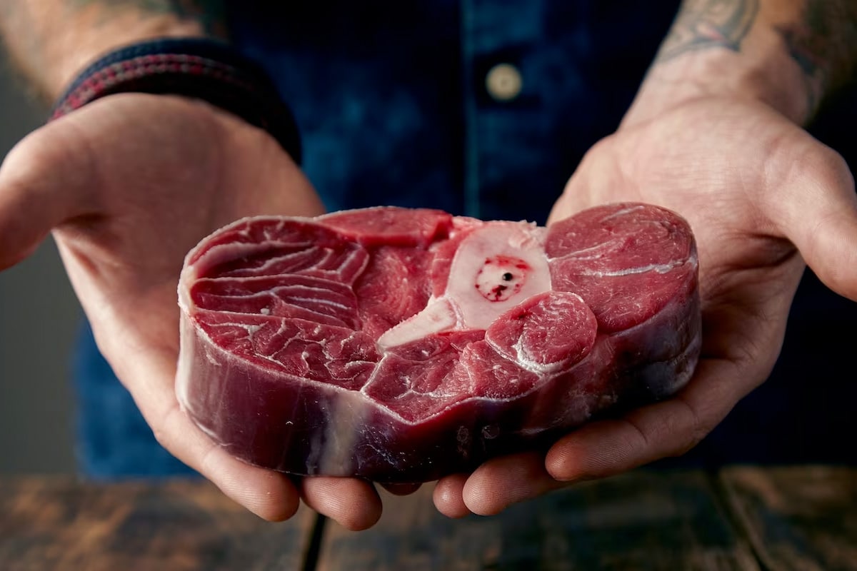 A tattooed butcher holding a pieces of raw meat in his hand.