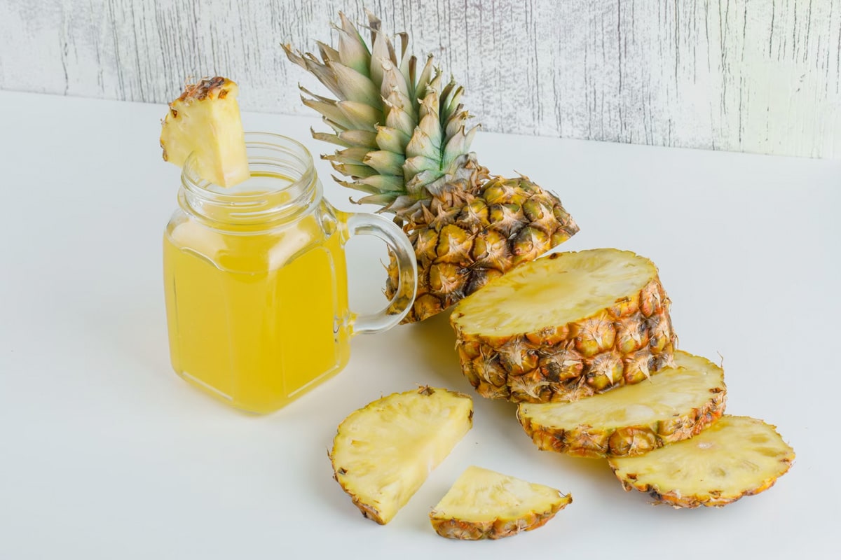 Close look of transparent jar with pineapple juice near a fresh pineapple slices.