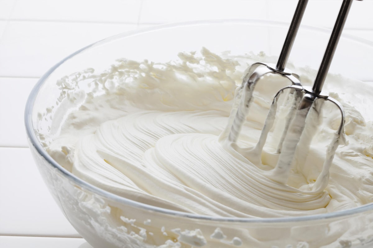 Making whipped cream using half and half in a transparent large bowl.