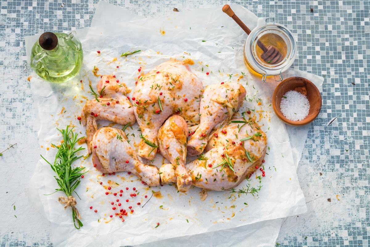 Marinated chicken legs with paprika, salt, and rosemary on parchment paper.