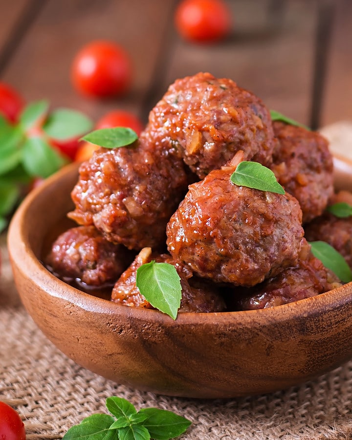 A wooden plate with cooked meatballs with some aromatic herbs on it.