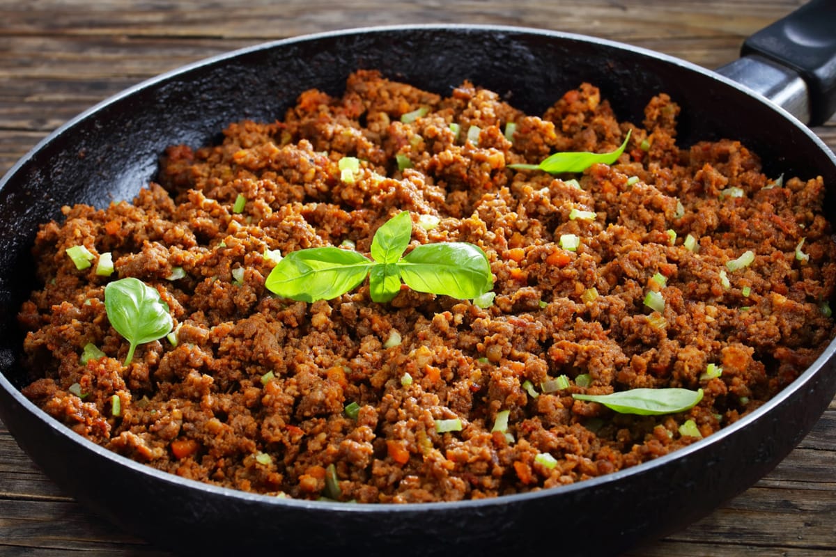 Close look of a black frying pan with cooked mince and a few leaves of basil.