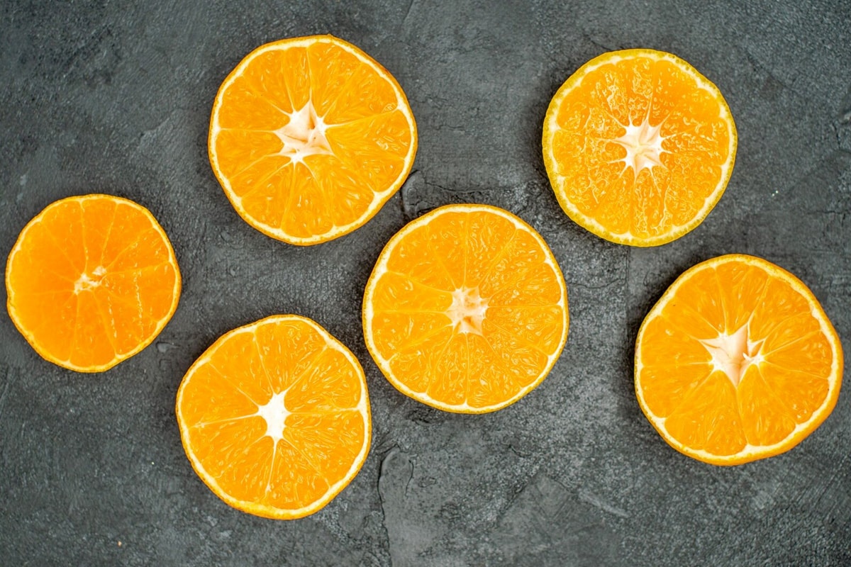 6 slices of seedless oranges on a dark concrete background.