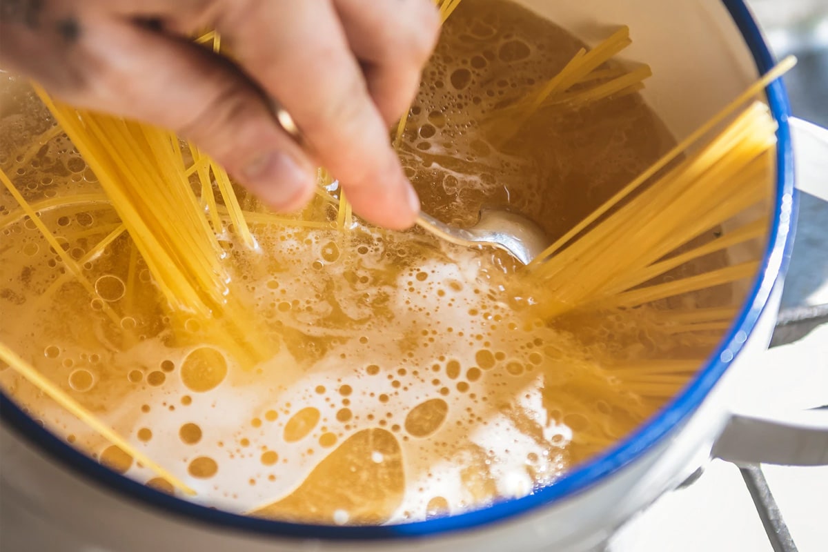 A hand mixing spaghetti in a pan with boiled water.