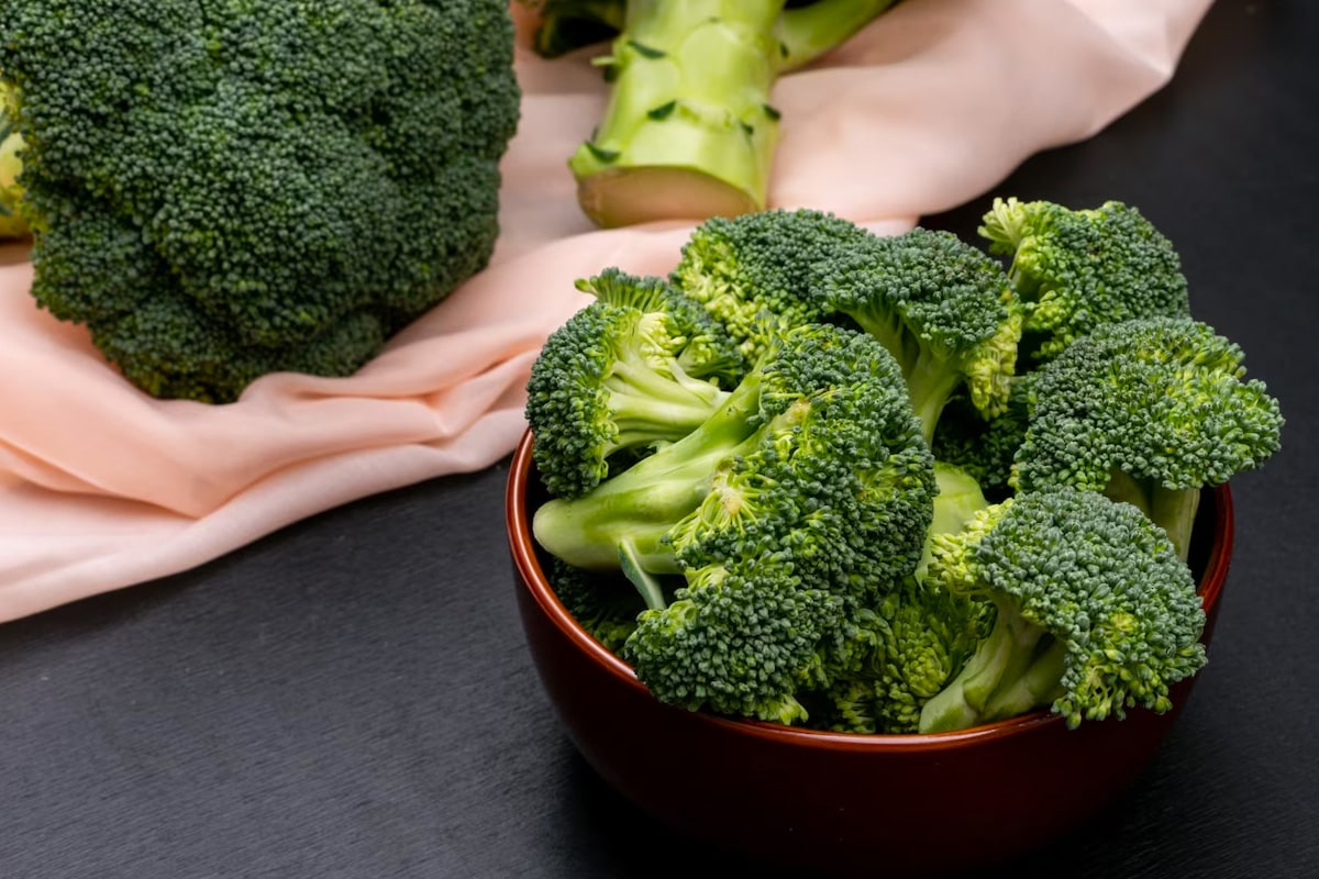 Close look of a red plate with broccoli florets in it on a dark table.