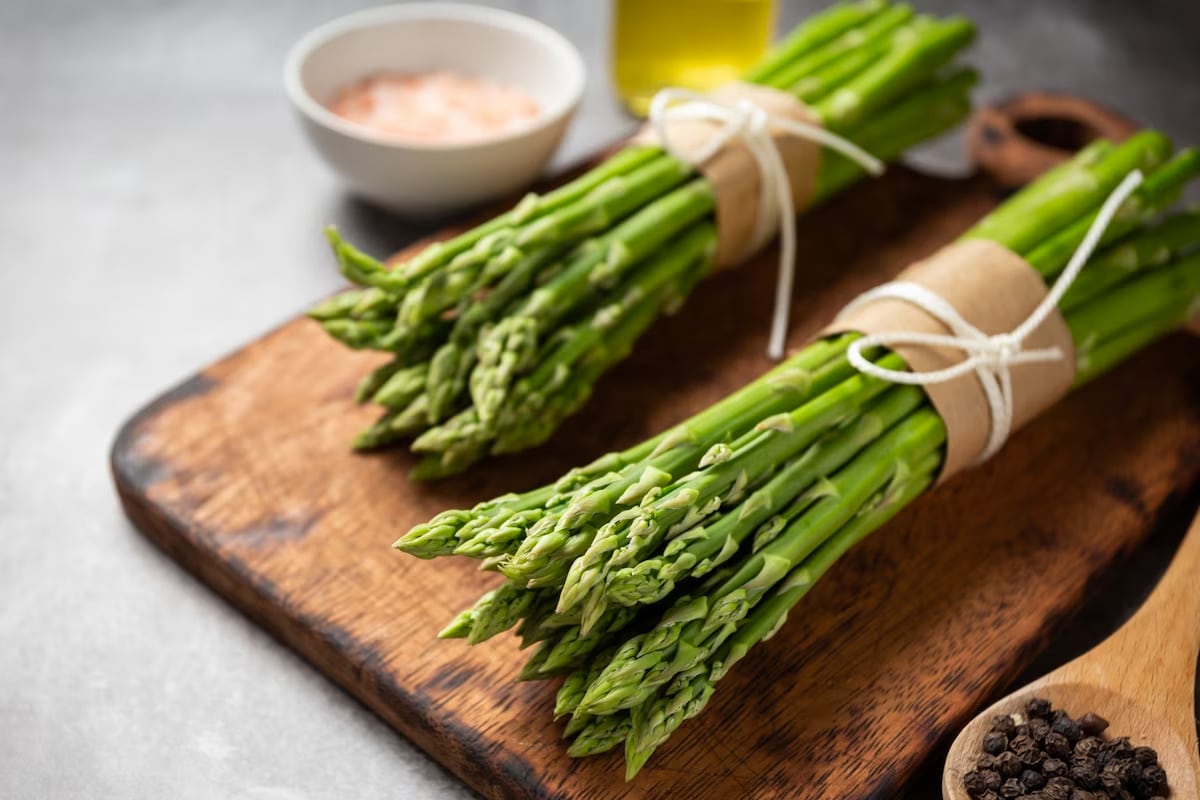 Two heaps of asparagus on a wooden cutting board.