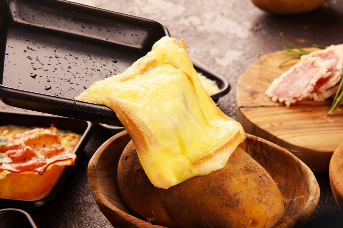 Close look of melted raclette cheese over a baked potato.
