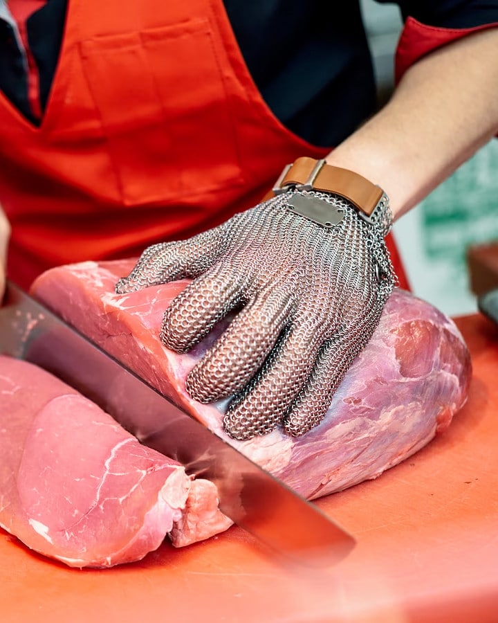 A butcher cutting meat steaks with a knife.