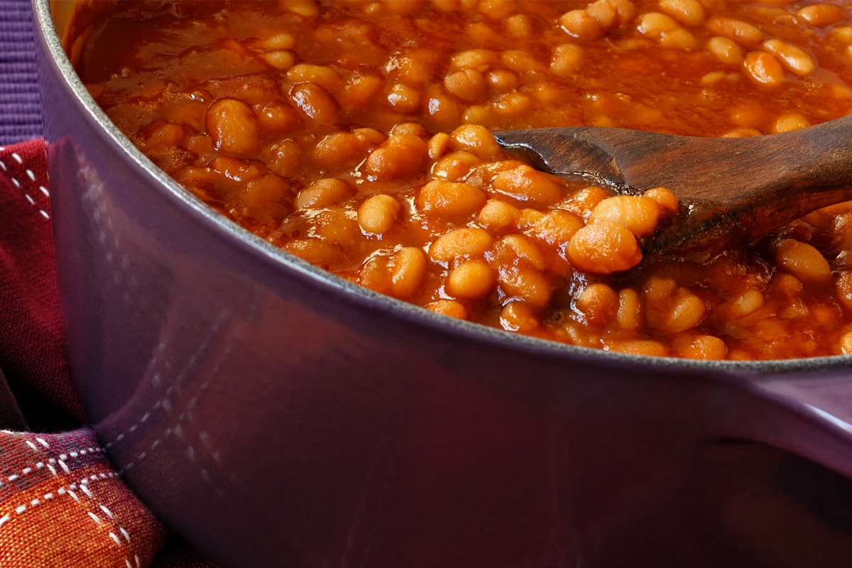 Close look of cooked beans in a purple saucepan with a wooden spoon in it.