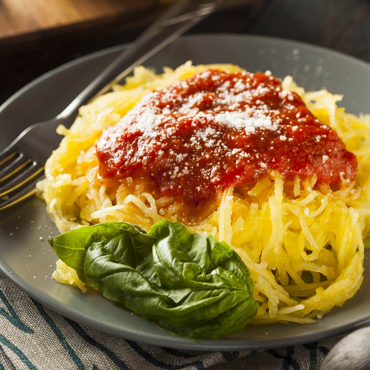 Close look of a gray plate with spaghetti squash, a basil leaf, and tomato sauce.