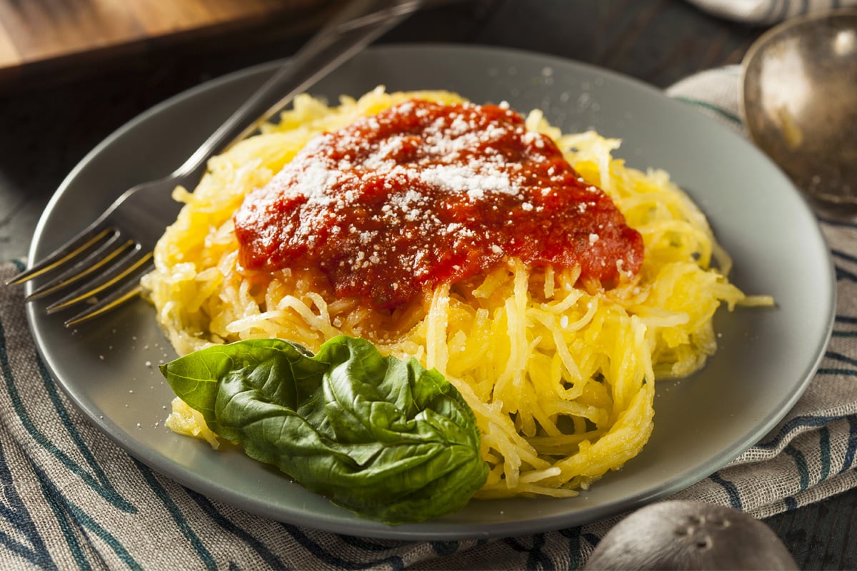 Close look of a gray plate with spaghetti squash, a basil leaf, and tomato sauce.