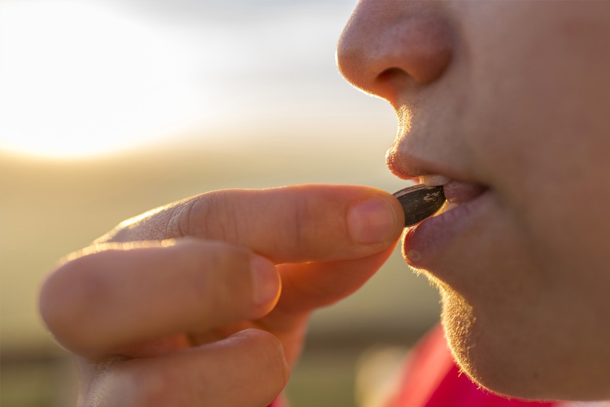 Close look of a woman's face eating sunflower seed with shells.