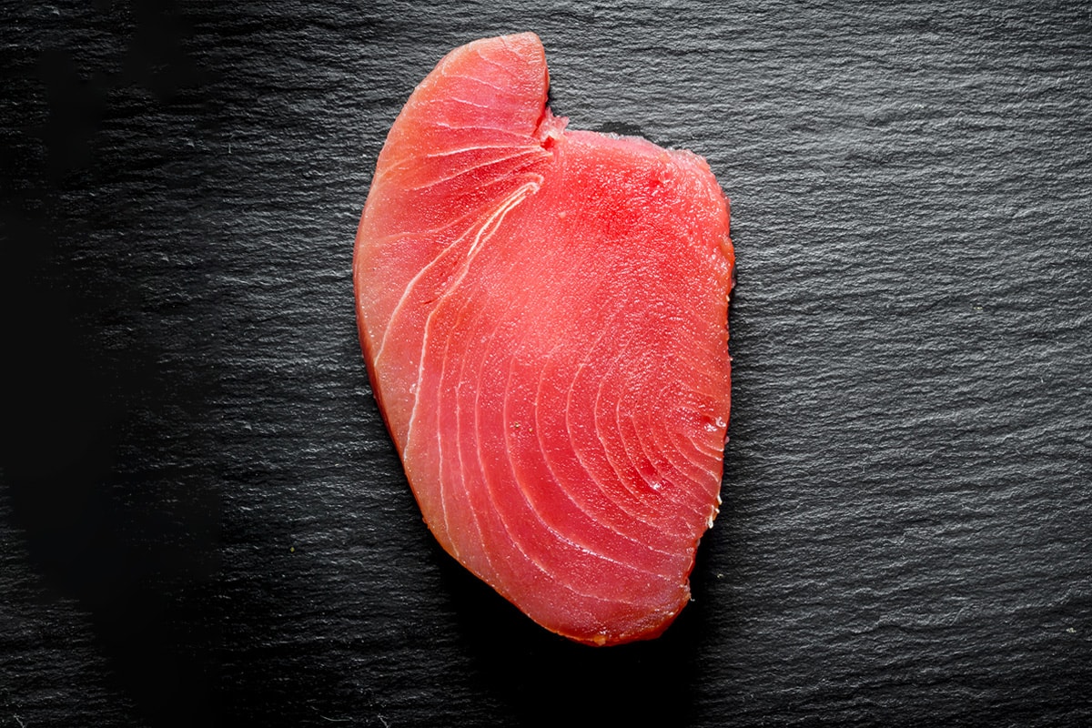 Top view of a slice of tuna meat on a dark table.