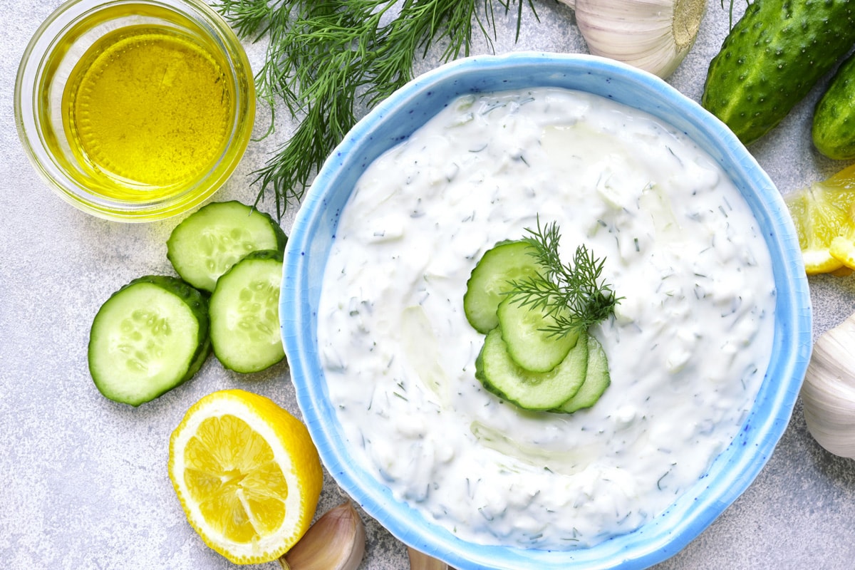 Top view of a blue plate with tzatziki sauce and 4 cucumber slices.