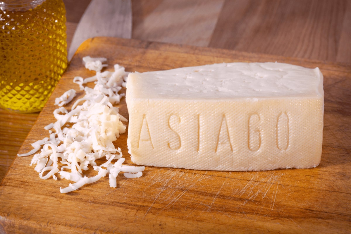 Piece of asagio cheese on a wooden cutting board.