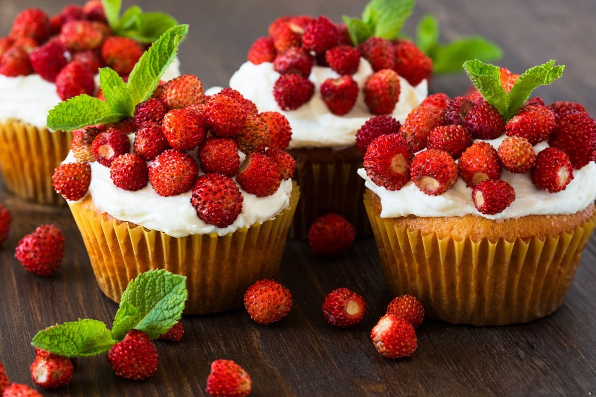 Close look of muffins with cream, wild strawberries and mint.