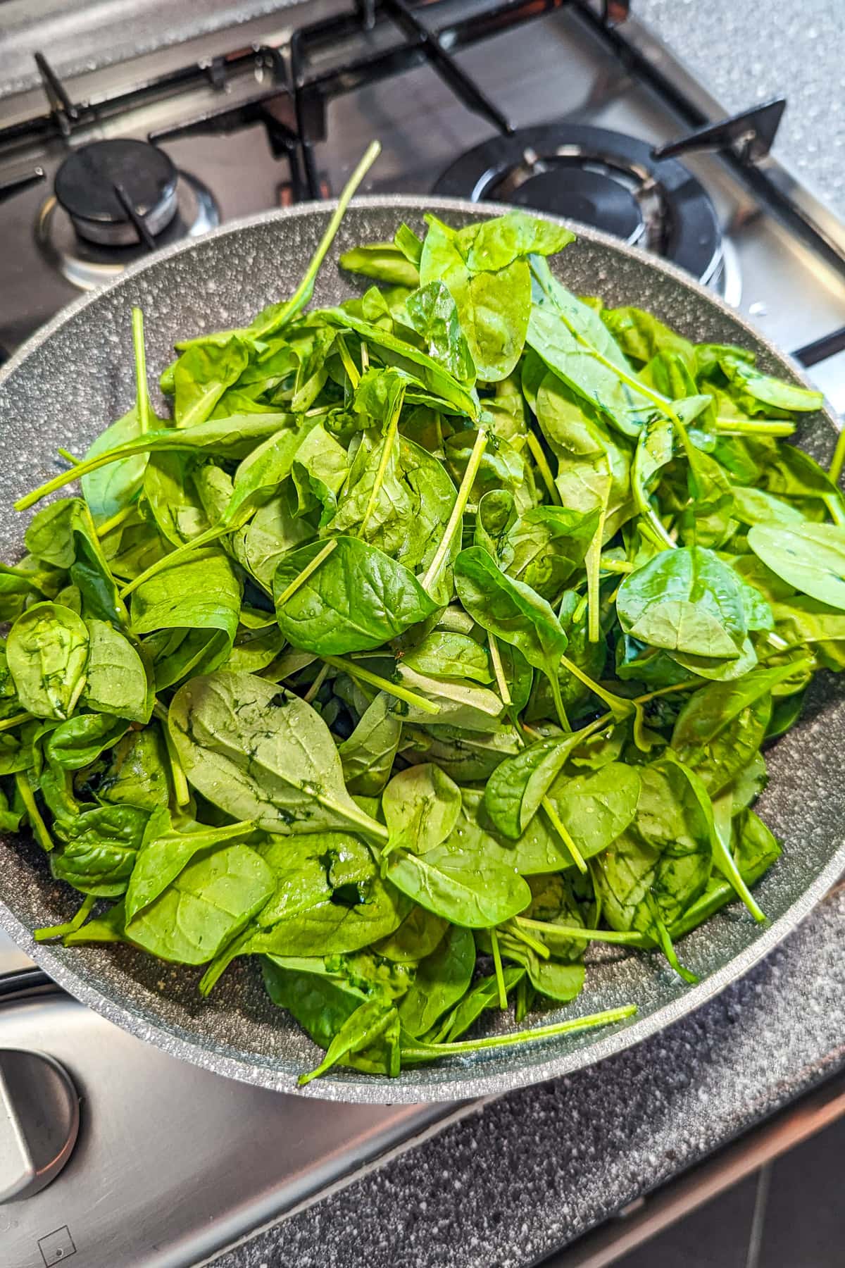 A frying pan full with uncooked spinach on the stove.