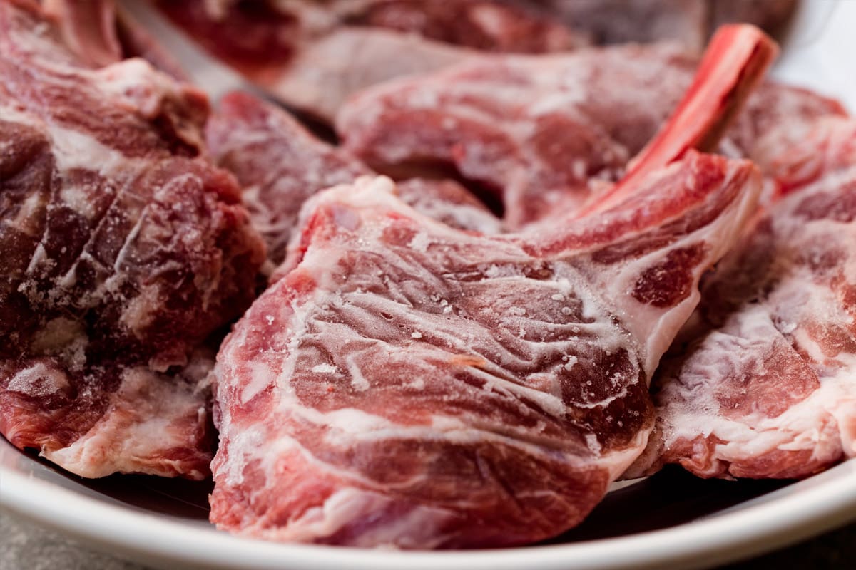 A white plate with frozen lamb chops.