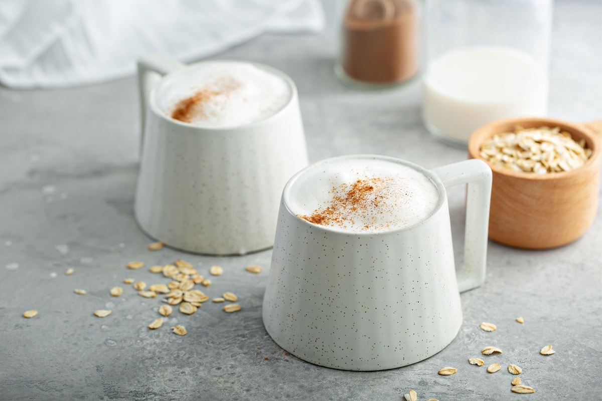 Two white cups with oatmilk, coffee and oats on the background.