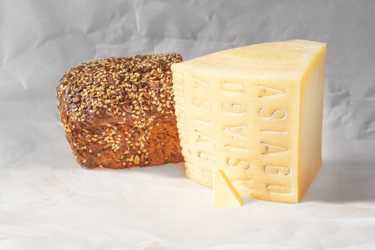 A piece of asiago cheese near a bread with seeds.