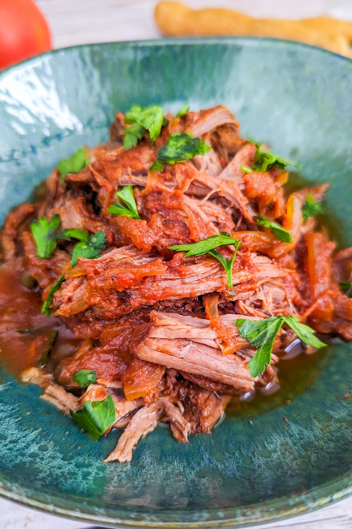 Close look of pulled beef with parsley in a green plate.
