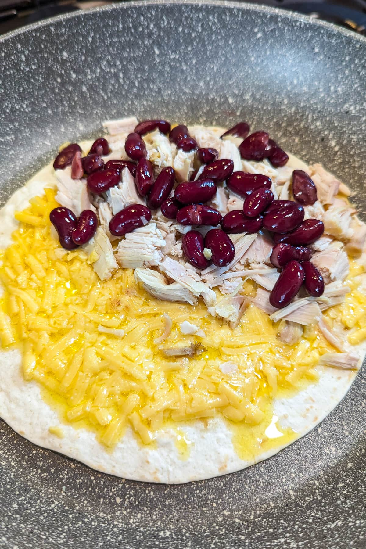 Frying pita with melted cheese, chicken and beans.