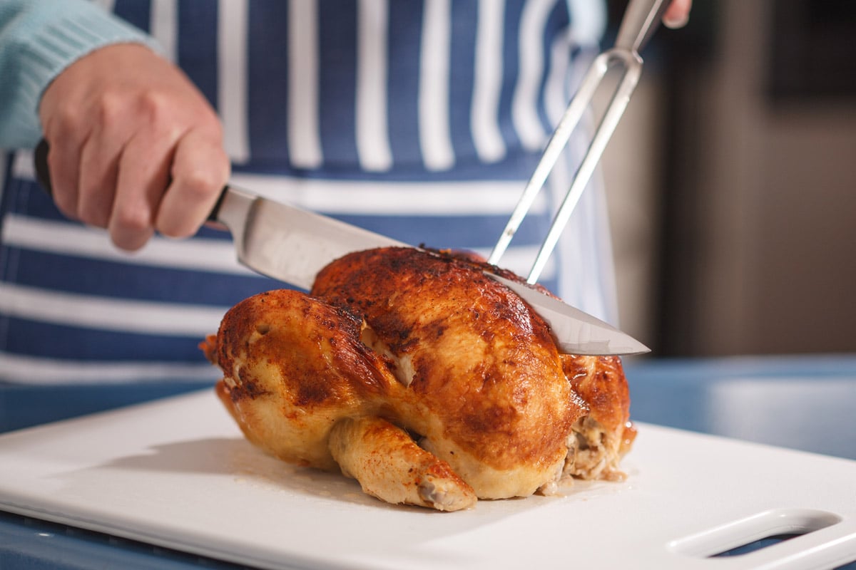 A woman with a knife and fork, slicing the rotisserie chicken.