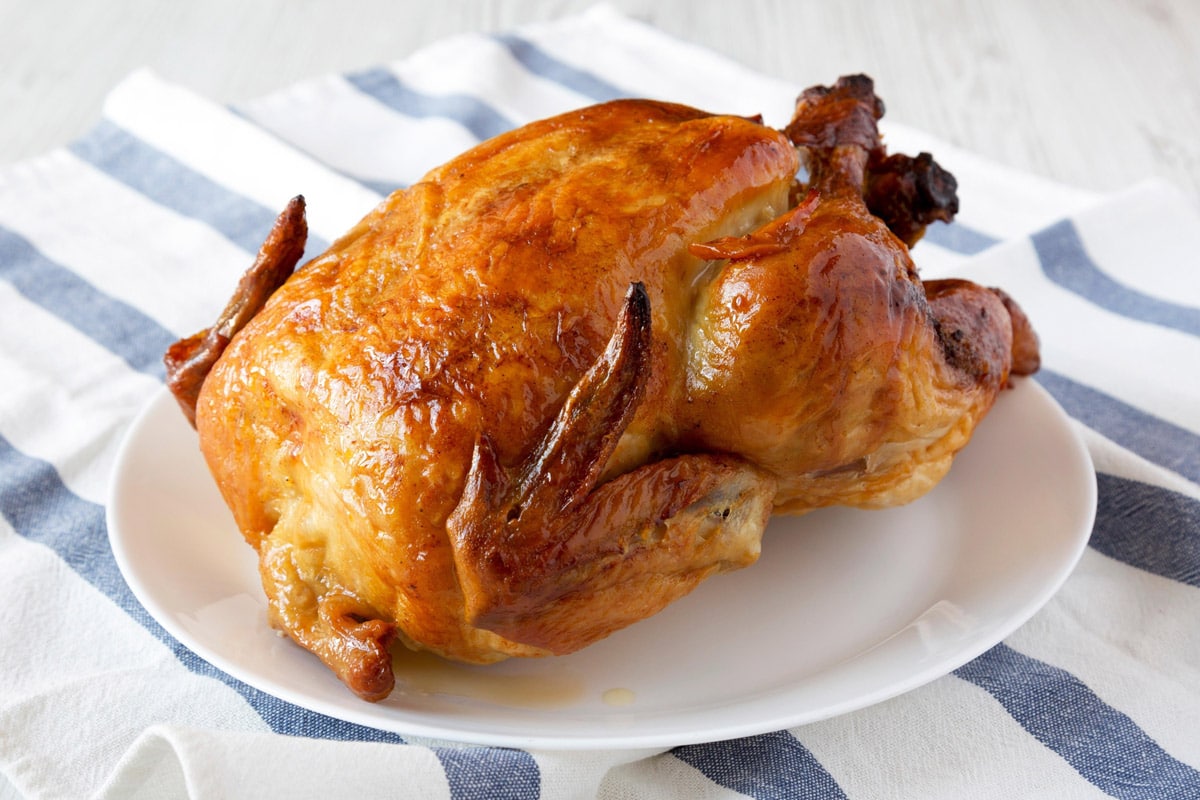 Close look of rotisserie chicken sitting on a white plate on a towel.