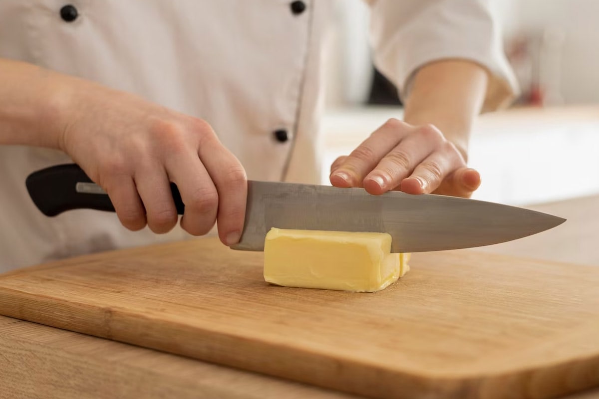 Chef with a knife slicing a piece of margarine on a wooden cutting table.