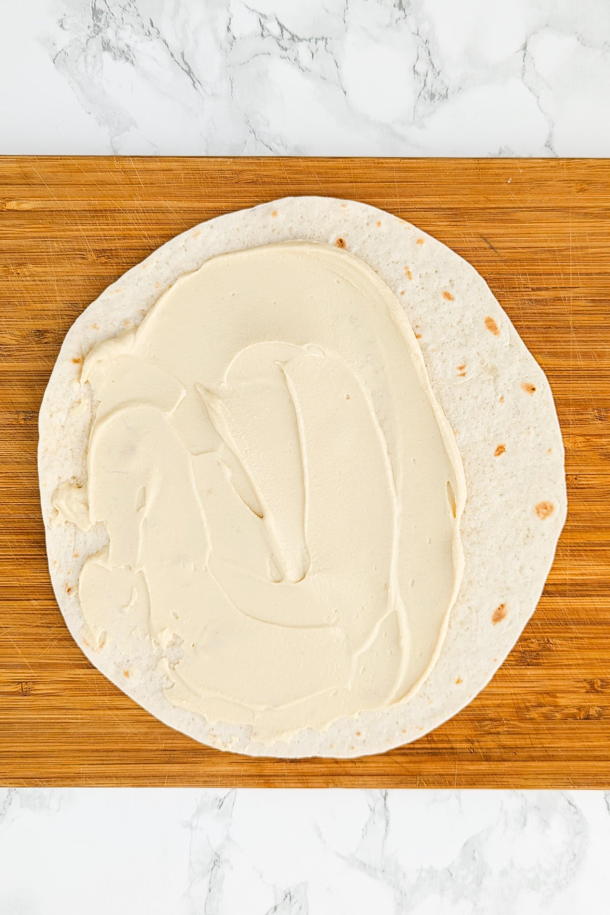 Top view of a wooden cutting board with a pita and cream on it.