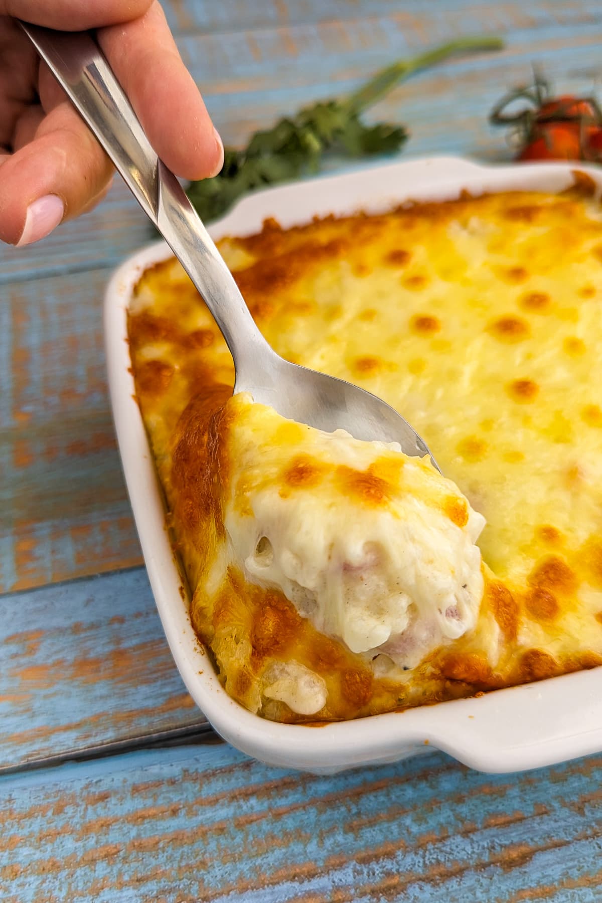A spoon with baked rice cheese over a baking dish.