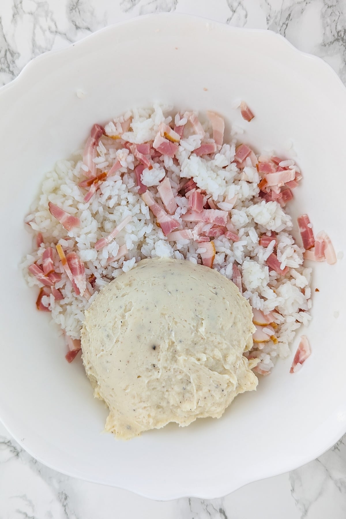 Cream, rice and ham in a white deep bowl on a white marble table.