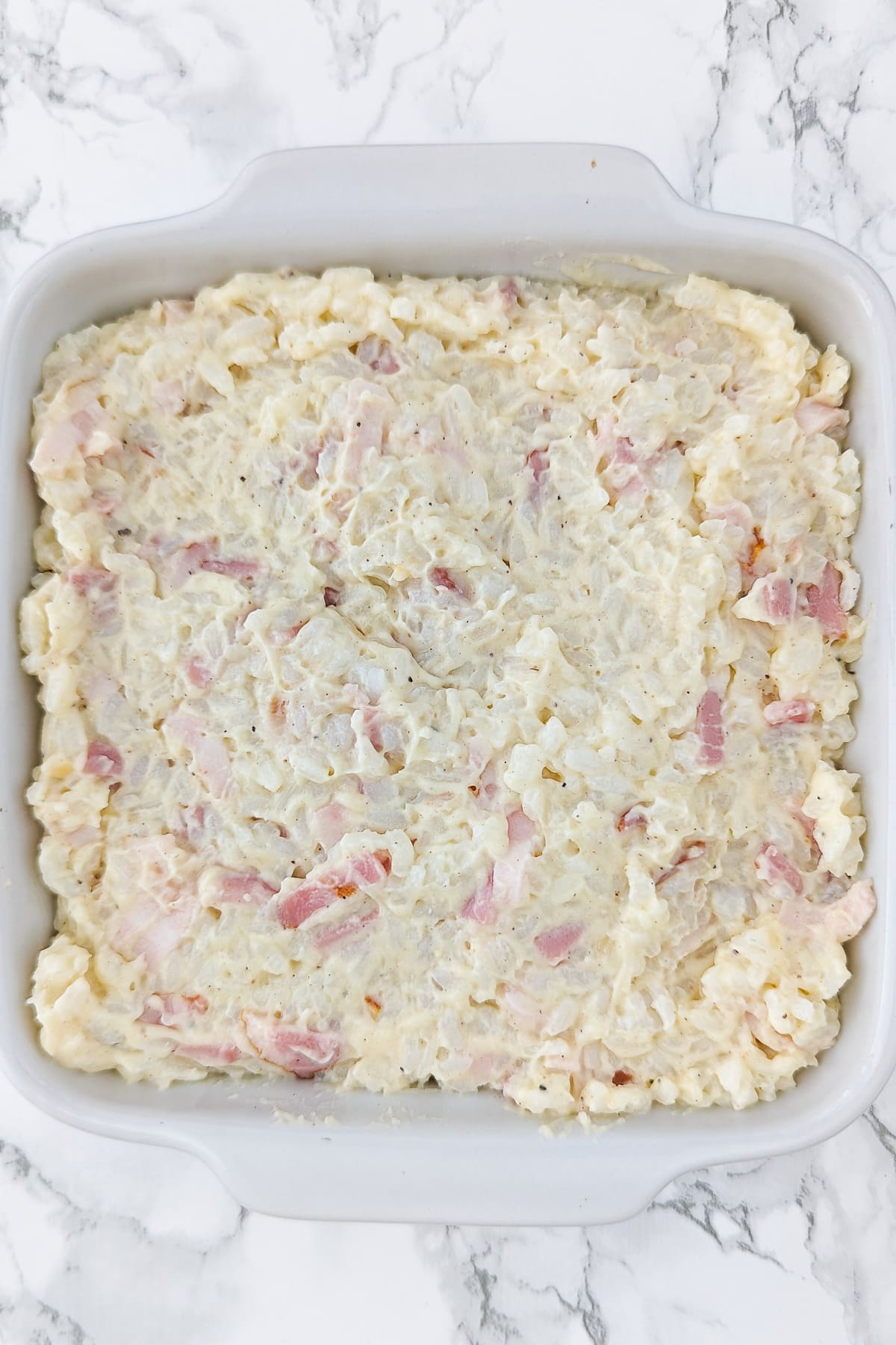 White baking dish filled with a mix of ham and rice on a white marble table.