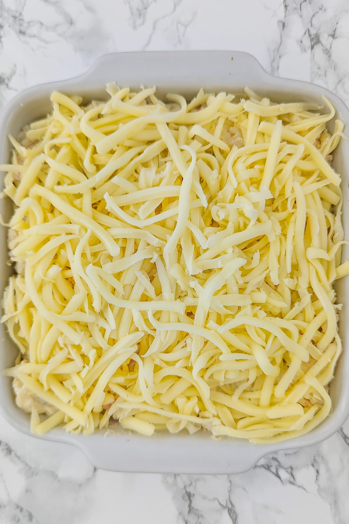 White baking dish topped with shredded parmesan cheese on a white marble table.