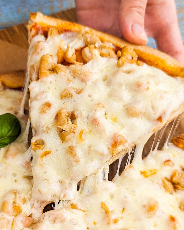 A woman hand holding a slice of beans pizza with melted cheese.