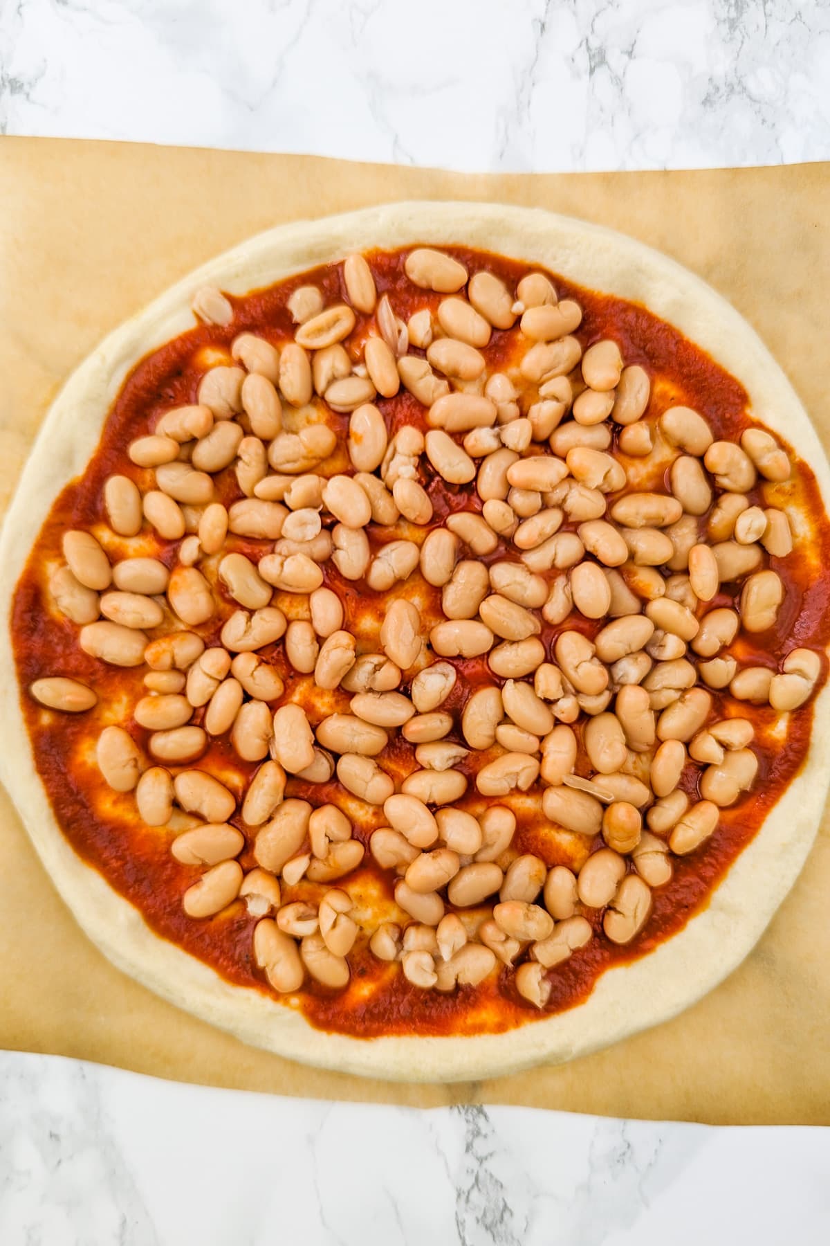 Top view of a raw pizza dough covered with pizza sauce and canned beans.