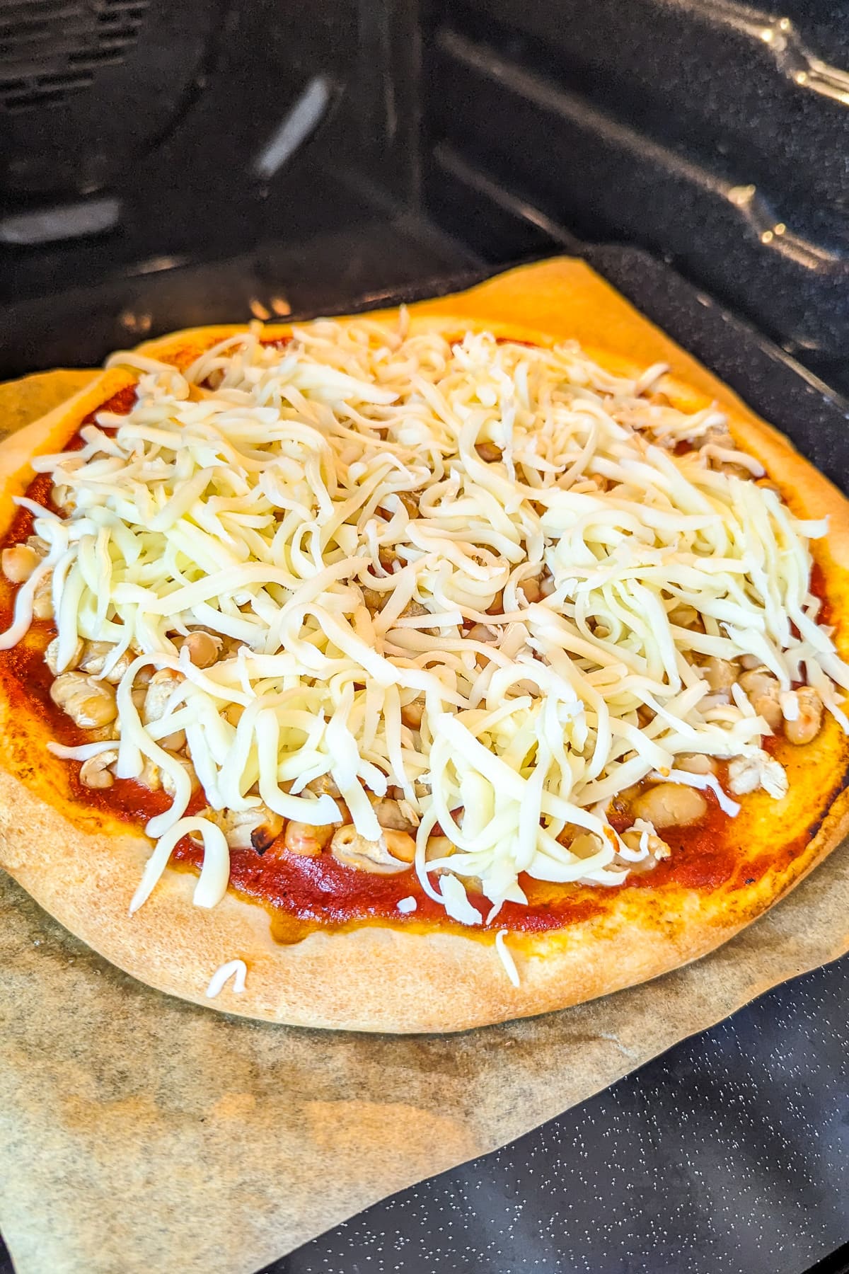 Adding shredded mozzarella cheese over a pizza sitting in the oven.