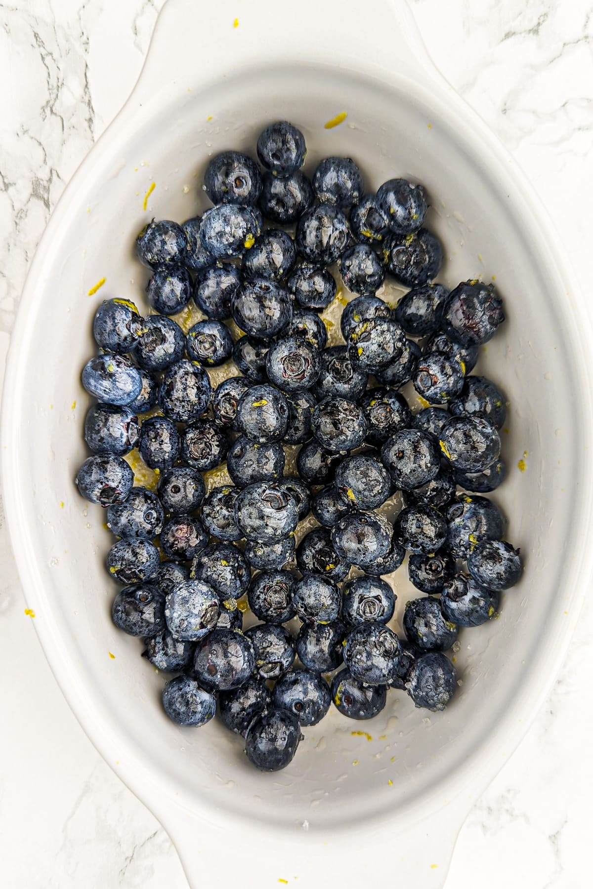 White baking dish filled with blueberries on a white marble table.