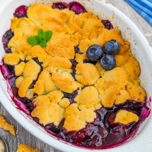 Close look of a blueberry cobbler decorated with 3 blueberries, and mint.