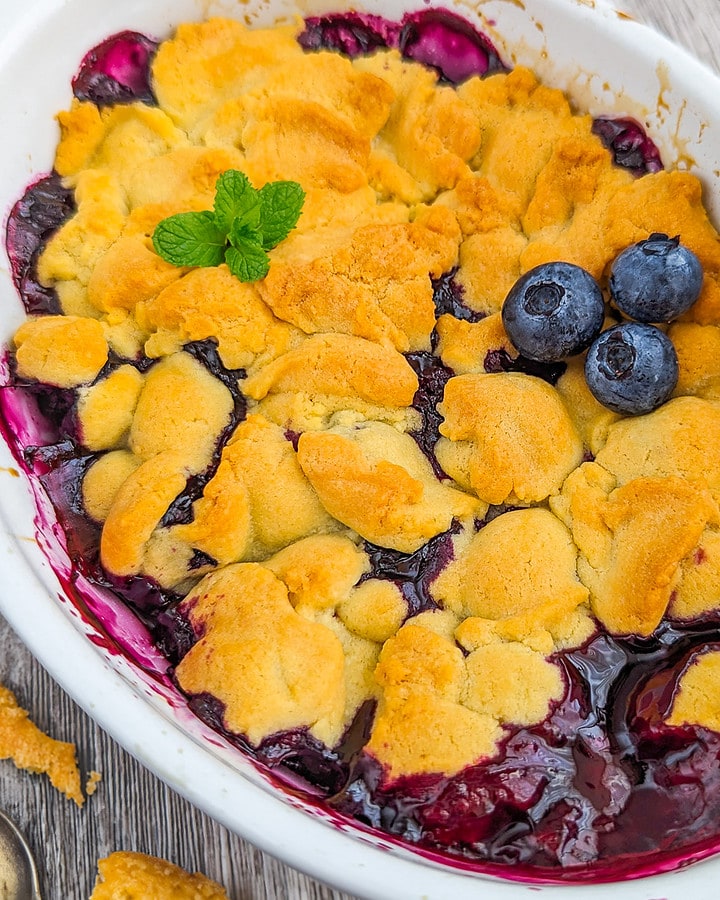 Close look of a blueberry cobbler decorated with 3 blueberries, and mint.