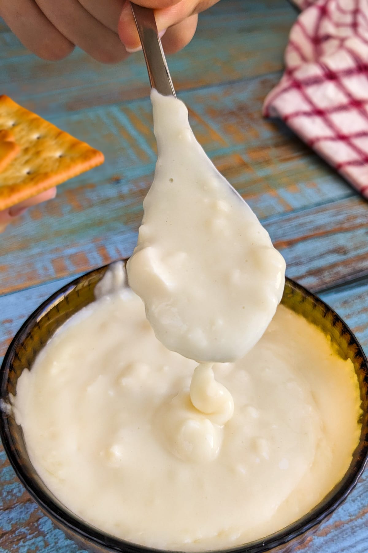 Woman hand pouring camembert sauce on a cracker.