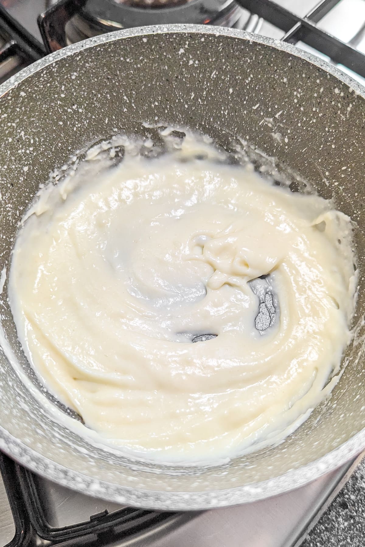 Mixed milk with flour and butter in a gray saucepan on the stove.