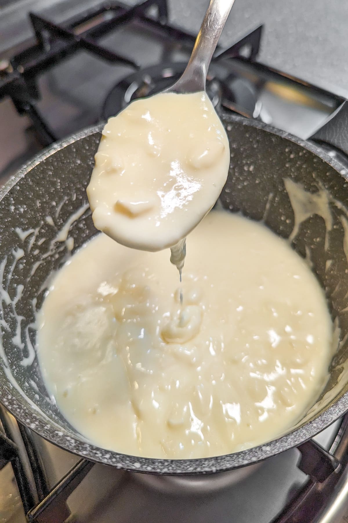 A spoon with camembert sauce over a saucepan on the stove.