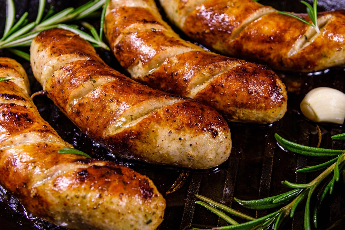 Close look of 4 fried sausages with aromatic herbs.