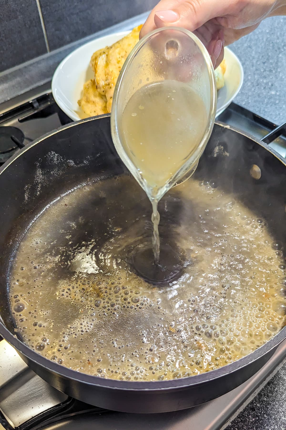 Pouring chicken broth in a pan on the stove.