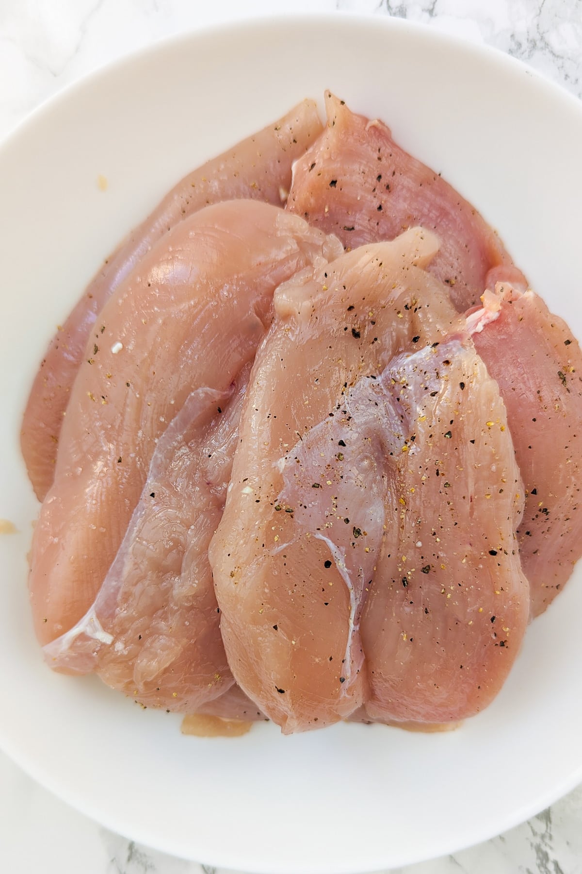 Top view of seasoned chicken breasts in a white bowl.