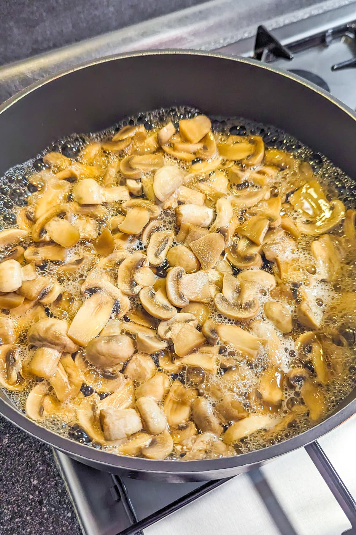 Frying pan with fried mushrooms, garlic and melted butter on the stove.