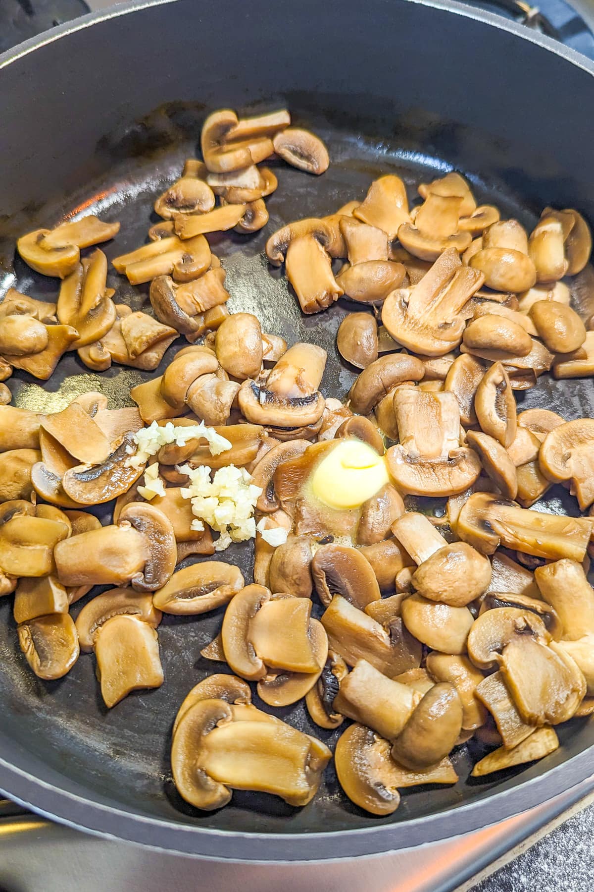Frying pan with fried mushrooms, garlic and melted butter on the stove.